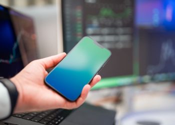 A person holding a smartphone with forex charts displayed, implying modern finance and technology.