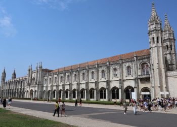 Explore the historic Jerónimos Monastery in Lisbon, Portugal, showcasing its detailed Gothic architecture under a clear blue sky.